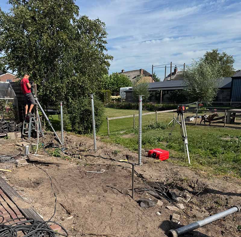 Overzicht plaatsing 10 schroeffunderingen voor tuinhuis in achtertuin Benschop met monteur op ladder