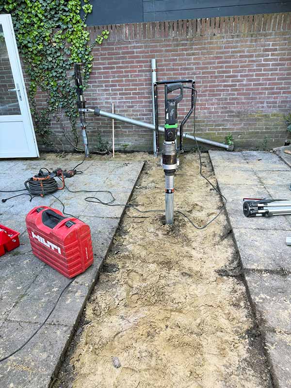 Hilti elektrische handmachine draait een V76 schroefpaal in de zandbodem langs de achtergevel, fundering voor aanbouw hoekwoning 's-Hertogenbosch