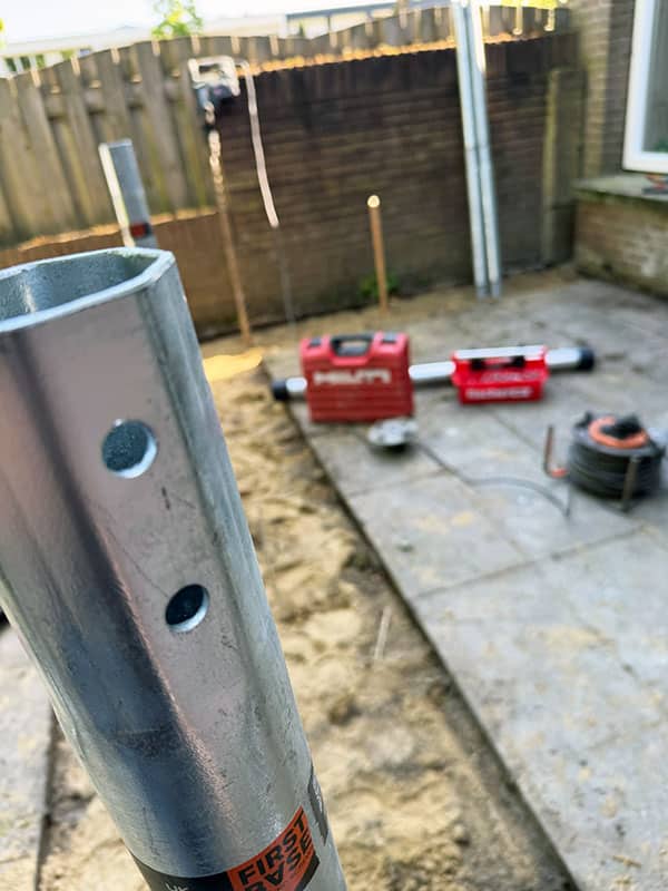 Close-up van een galvanische V76 schroefpaal in de zandbodem, met Hilti-handgereedschap op de achtergrond, voorbereiding fundering aanbouw hoekwoning 's-Hertogenbosch