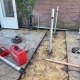 Twee geplaatste V76 schroefpalen steken uit de zandbodem langs de achtergevel, klaar als fundering voor de aanbouw van een hoekwoning in 's-Hertogenbosch