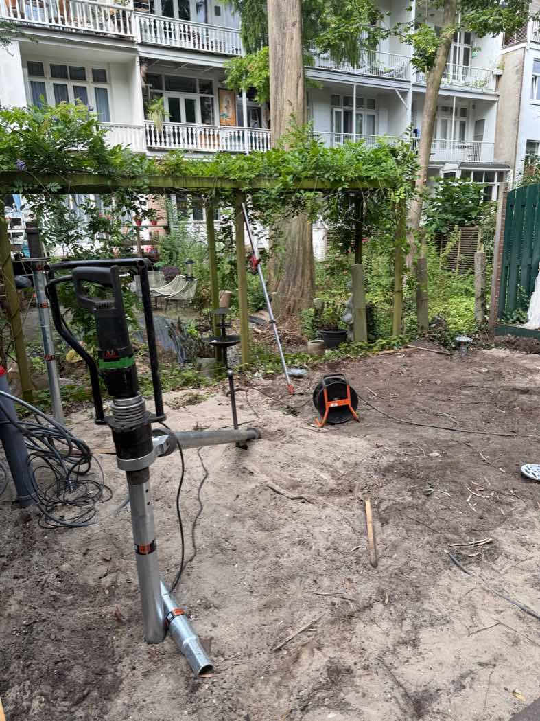 Handmachine van Van Aken voor het plaatsen van schroefpalen in een Amsterdamse binnentuin, met op de achtergrond de karakteristieke achtergevels en balkons